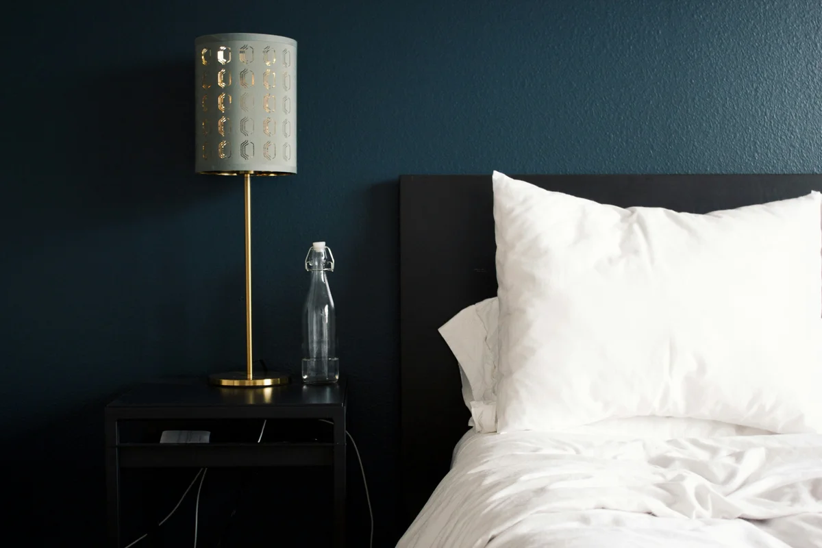 Hotel bedside detail with decorative brass lamp, water bottle, and crisp white pillows