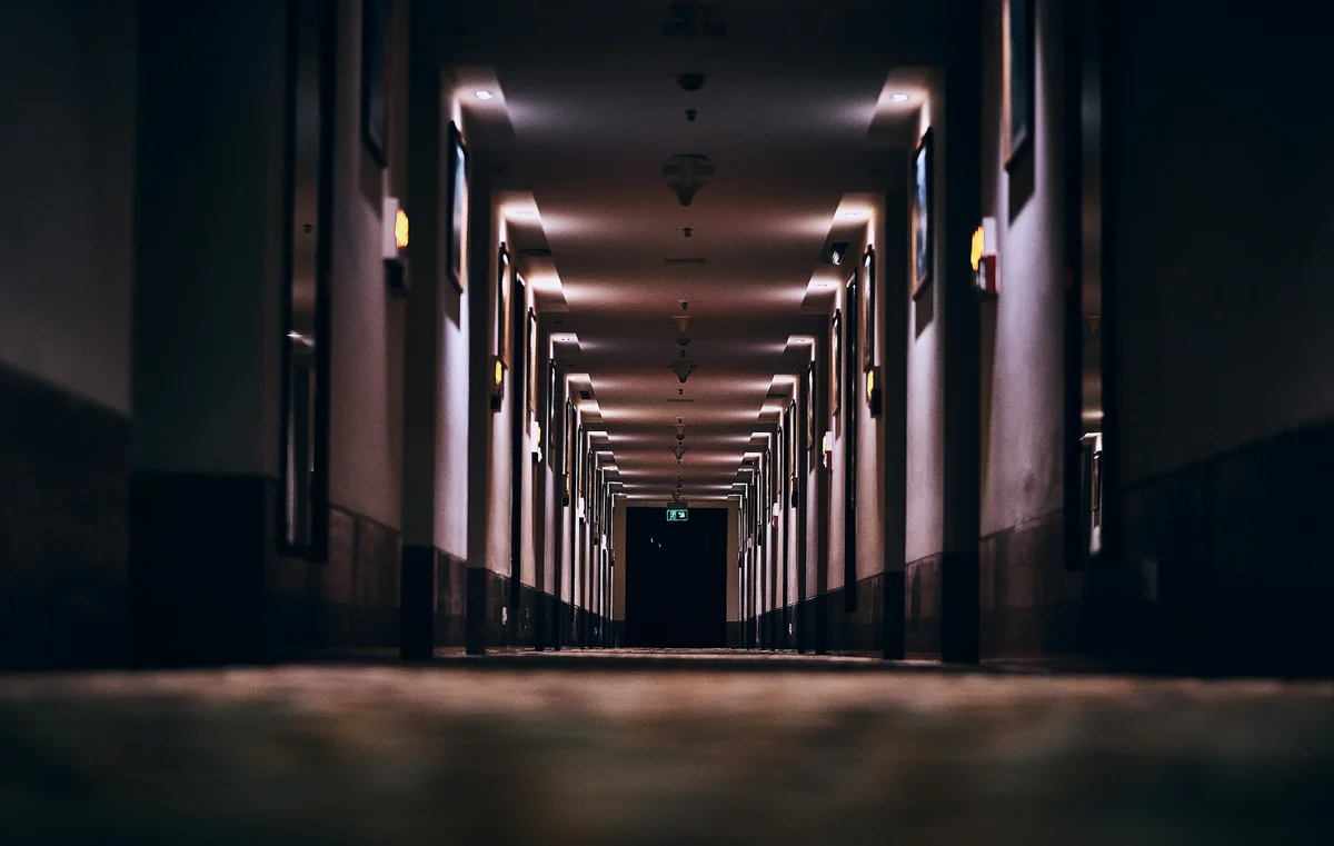 Dimly lit hotel corridor at night with wall sconces and exit sign