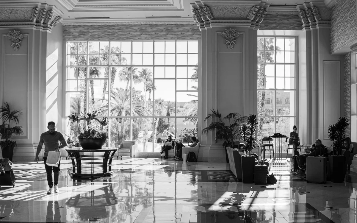 Grand hotel lobby with tall windows, marble floors, and staff walking through