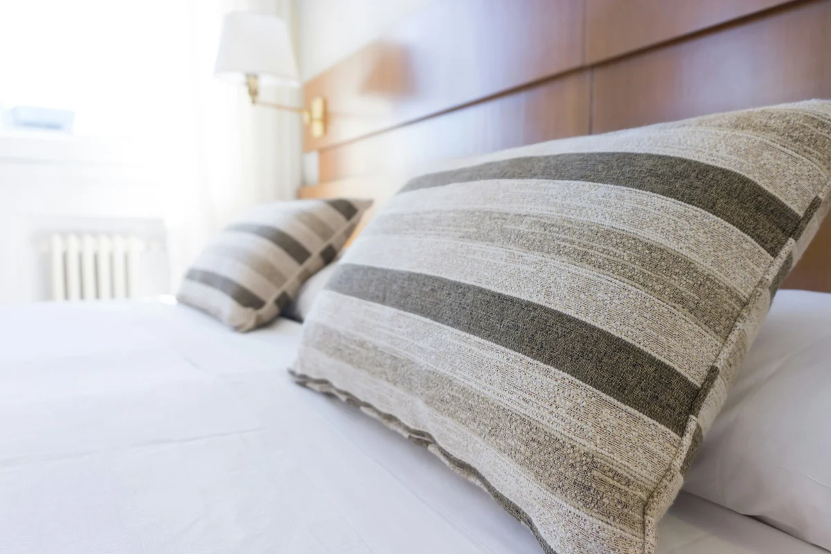 Hotel bed close-up with striped decorative pillows and sunlit white linens