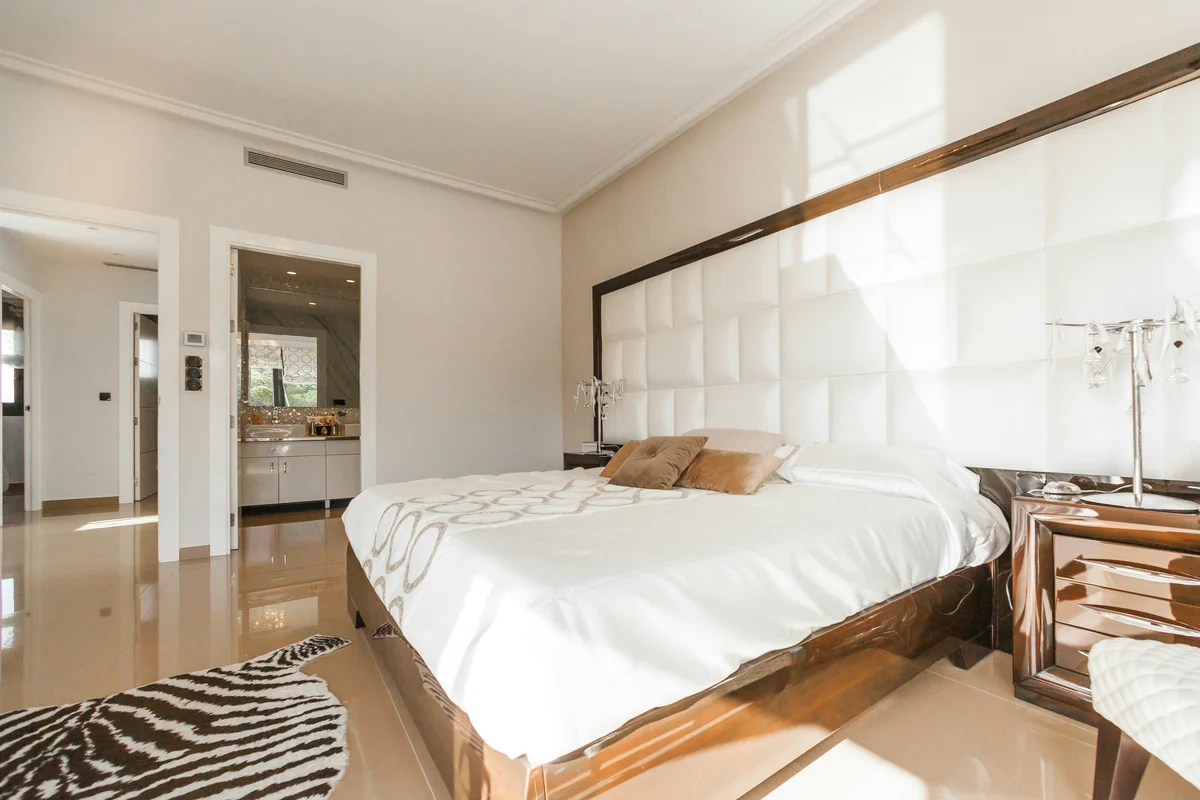Luxury hotel suite with padded headboard, mirrored nightstands, and en-suite bathroom